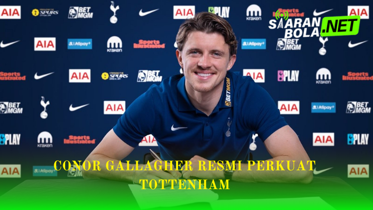 Conor Gallagher tersenyum saat menandatangani kontrak mengenakan polo shirt biru gelap dengan latar belakang logo Tottenham Hotspur dan sponsor, terdapat teks Conor Gallagher Resmi Perkuat Tottenham dan logo SiaranBola.net.