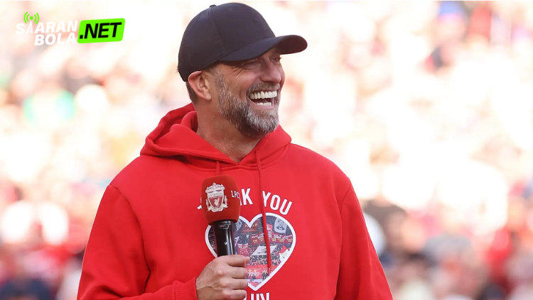 Jürgen Klopp mengenakan jaket hitam dan topi Liverpool sambil melakukan selebrasi di pinggir lapangan saat pertandingan berlangsung.